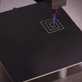 Video still of a robot arm applying adhesive to a panel in a spiral square pattern