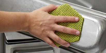  A worker cleans a stainless steel pan with a Scotch-Brite™ HEX Series sponge.
