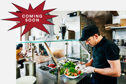 A restaurant worker prepares a salad while wearing food service gloves.