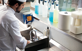 male chef washing his hands with disinfectant bottles displayed in background.