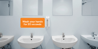 An orange wall graphic above the sinks in a public restroom reads “Wash your hands for 20 seconds.”
