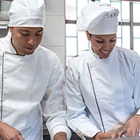 Two chefs in white coats confer in a commercial kitchen