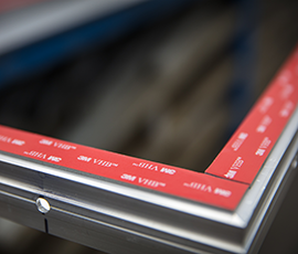 Closeup image of 3M™ VHB™ Tape applied to a metal frame before the liner is removed and the panel attached