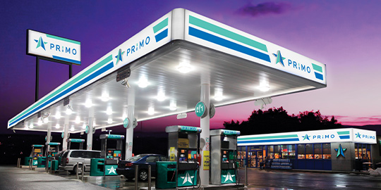 Gas station with illuminated exterior signage and purple sky in background.
