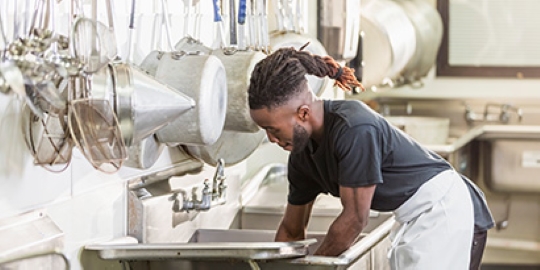 A man washes dishes in a commercial kitchen.
