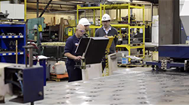 Still shot of workers at a production line machine control panel at WS Steel