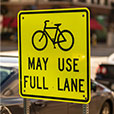 Yellow road sign with image of bicycle and words “may use full lane.”