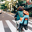 Adult riding bicycle with small child in child seat on urban road near crosswalk.