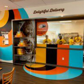 Interior restaurant window with wall and floor graphics and two workers behind the window.