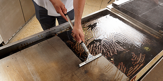Commercial kitchen worker using 3M Quick Clean griddle cleaning squeegee to clean griddle.
