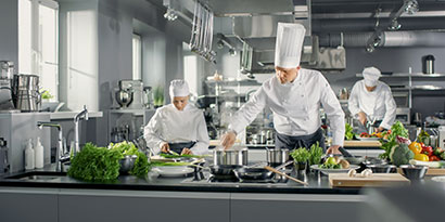 Three chefs prepare fresh vegetables in a commercial kitchen.
