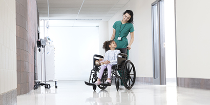 female health care professional pushing a young patient in a wheelchair
