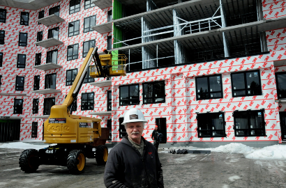 Image of a man standing on a job site with snow and a building partly wrapped with a 3M air barrier