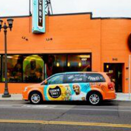 Minivan with colorful car wrap, parked in front of building with window wraps.
