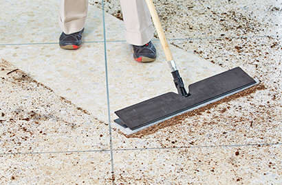 A worker using 3M Easy Trap dusting tool to clean dirt off a floor.
