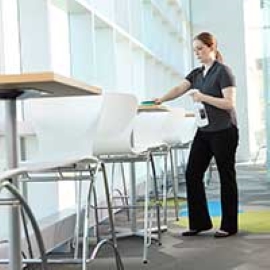 A restaurant worker cleans a table with a sponge and cleaning solution.