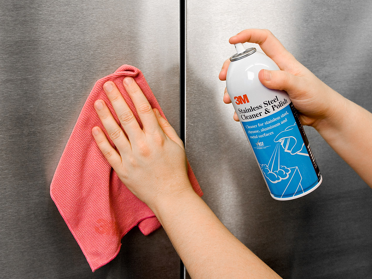 A kitchen worker using 3M scrubber to clean stainless steel pot.
