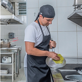 A commercial kitchen worker scrubs a pan at a sink.