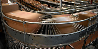 Image of blurred cartons moving at speed around a bend on a conveyor system
