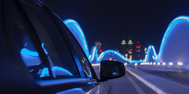 Electrified car driving in a city at night. Illuminated city in the foreground.