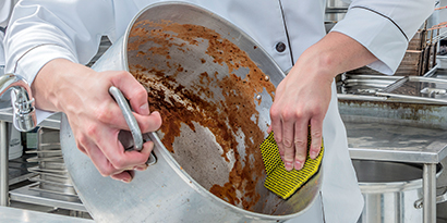 A kitchen worker cleans a large pot with Scotch-Brite™ Dual Purpose Scour Pad 96HEX.
