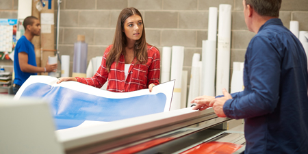 A woman and a man inspect printed sign sheeting in a shop.
