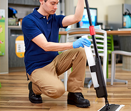 A worker assembling a spray mop with a gloved hand.
