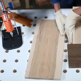 Video still of a worker holding a drawer slide in place after attaching with the hot melt gun on a stand at left
