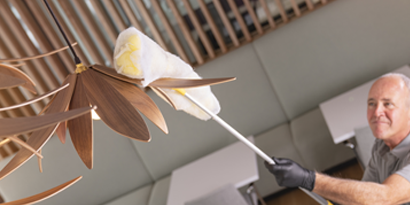 man using a high dusting tool wrapped with a 3M easy trap sweep and dust sheet to clean a commercial pendant light
