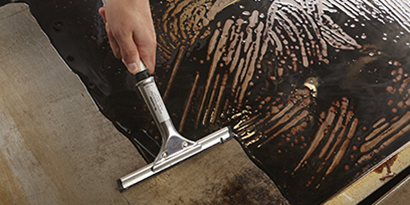 A commercial kitchen worker cleans a flat-top griddle with a Scotch-Brite™ Squeegee.
