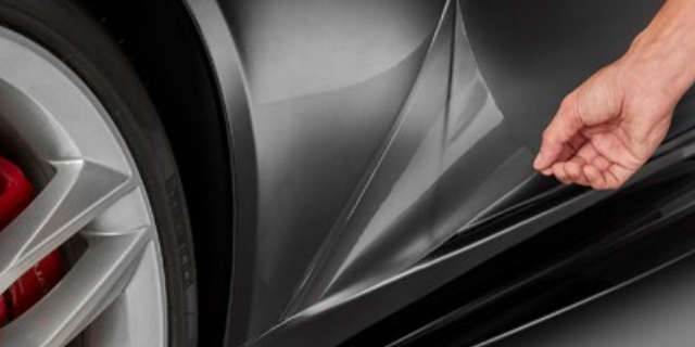 Person installing clear 3M paint protection film on sedan door.