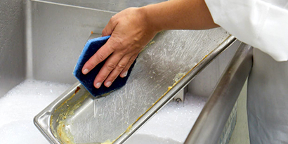 A kitchen worker cleans a pan with Scotch-Brite™ Low Scratch Scour Pad 2000HEX.
