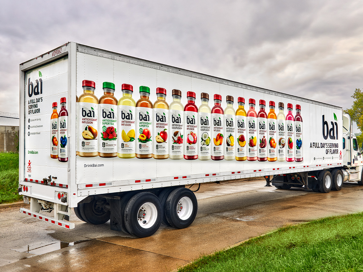 Delivery van with vehicle wrap in front of exterior wall with large graphic wrap showing picture of vegetables.
